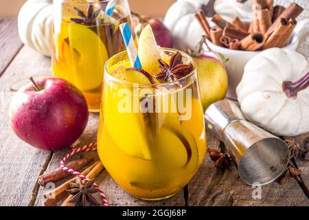 Boozy Pumpkin Party Punch, sangria di ringraziamento con succo di zucca, mela, pera e spezie, fondo in legno accogliente con maglione caldo e ingredienti c Foto Stock