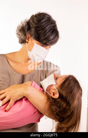 madre e figlia che indossano maschere protettive su sfondo bianco Foto Stock