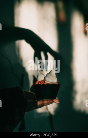 Colpo verticale di un'impostazione di Halloween spettrale, un cupcake con l'ombra della mano di una strega sopra di esso Foto Stock