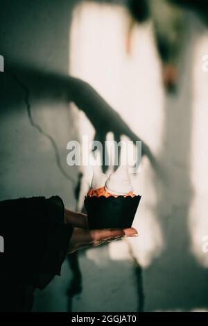 Colpo verticale di un'impostazione di Halloween spettrale, un cupcake con l'ombra della mano di una strega sopra di esso Foto Stock