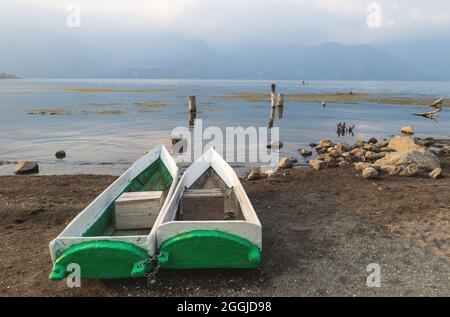 Canoe pescatori tradizionali sulla riva lungo il lago Atitlan durante il tramonto con vista sulle nebbie montagne vulcaniche a San Pedro la Laguna, Guatemala Foto Stock