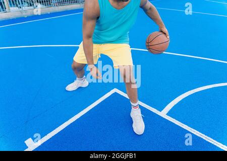 Vista ritagliata di un giovane afro americano irriconoscibile sul campo di pallacanestro strada che dribbling con la palla. Foto Stock