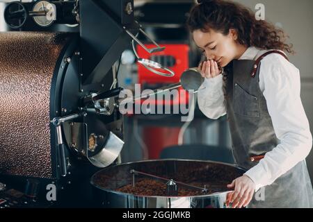 La macchina tostatrice e il barista odorano i chicchi tostati durante la tostatura del caffè. Foto Stock