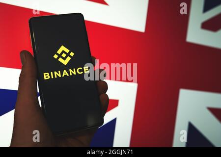 Logo Binance app sullo smartphone in mano con lo sfondo sfocato della bandiera British Union Jack. Binance nel Regno Unito notizie. Crypto Exchange, piattaforma di trading. Swansea, Regno Unito - 29 agosto 2021. Foto Stock