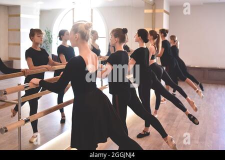 Vista laterale gruppi di ragazze che eseguono esercizi al bar in palestra con un focus sull'atletismo in un concetto di salute e fitness. Foto Stock