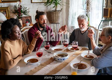 Famiglia e concetto religioso. Gruppo di persone multietniche con cibo che prega prima del pasto Foto Stock