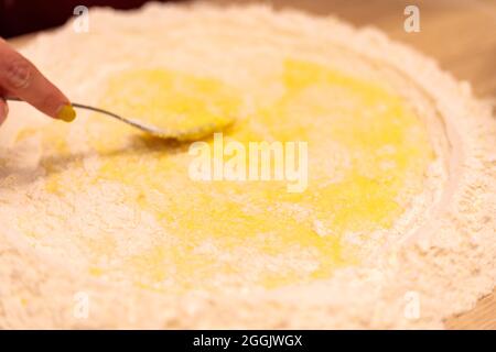 Una mano femminile con una forchetta impasta la pasta. Mescola l'uovo crudo con la farina. Primo piano. Foto Stock