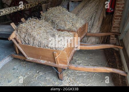 Genk, Belgio - 11 agosto 2021: Domein Bokrijk. Coppia di carriole in legno beige caricate con paglia secca in stalla. Foto Stock