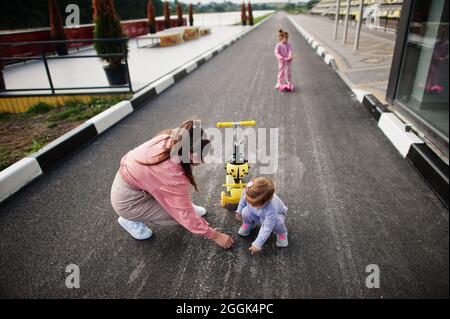 Giovane madre elegante con due ragazze all'aperto. La famiglia sportiva può trascorrere del tempo libero all'aperto con gli scooter. Dipinto con gesso sull'asfalto. Foto Stock