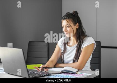 Un giovane studente studia online. Lavoratore di ufficio. Donna d'affari che lavora in ufficio. Comodo luogo di lavoro. Lavoro a distanza. Guadagna denaro extra Foto Stock