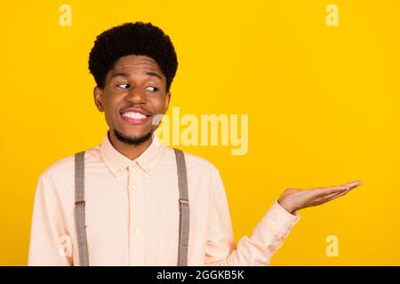 Photo ritratto uomo con capelli ricci mantenendo spazio vuoto sulla palma sorridente felice isolato vibrante colore sfondo giallo Foto Stock