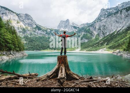 Un viaggiatore felice che si erge su un'altura ammirando le montagne di Dachstein su un lago Upper Gosau. Gosau, Salzkammergut, Austria, Europa. Foto Stock