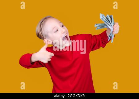 il bambino felice tiene le banconote in mano e dà i pollici in su Foto Stock