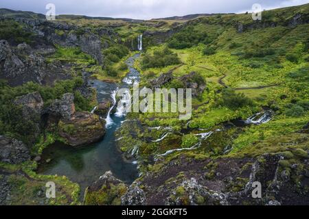 Cascata delle cascate di Gjain, colorata valle delle rocce laviche, lussureggiante muschio verde e vegetazione e corsi d'acqua blu nel sud dell'Islanda Foto Stock