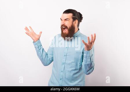 Il ippster bearded che indossa la camicia blu chiara è urlare e le braccia di tenuta si aprono largo su sfondo bianco. Foto Stock