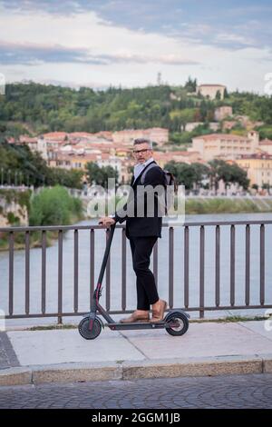 Bel uomo d'affari in tuta a guidare uno scooter elettrico mentre si viaggia per lavoro in città. Concetto di trasporto ecologico Foto Stock