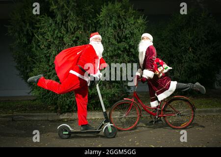 Riunione di due clausole di Santa. Babbo Natale guida uno scooter. Il Moroz della Russia passa in bicicletta. Le clausole di Babbo Natale hanno fretta di consegnare regali. Foto Stock