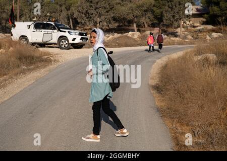 Dal 2004 i bambini del villaggio di Tuba stanno andando a scuola nel vicino villaggio di AT-Tuwani, 2.6 km di distanza - mentre sono stati condotti da un attivista ebraico e un veicolo delle forze di difesa israeliane per proteggerli dagli attacchi violenti da parte dei coloni ebrei religiosi dall'avamposto illegale di Maon Farm, che si trova sul loro cammino verso la scuola. Palestina / Israele, a sud di Hebron. 31 agosto 2021. (Foto di Matan Golan/Alamy Live News) Foto Stock