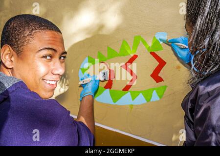 Miami Florida,volontariato volontario che lavora aiutando,Martin Luther King Jr. Giorno di servizio,MLK studente Black boy teen teenager murale pittura sorridente Foto Stock