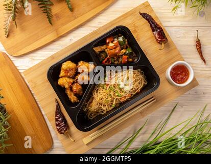 Posa piatta di tagliatelle con stufato di pollo e cubetti di pollo impanati in scatola da take-out sul tagliere di bambù Foto Stock