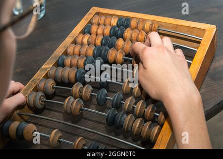 Mano femminile contando su antico vecchio abaco retrò, sfere in movimento su uno sfondo di legno, primo piano. Concetto commerciale e finanziario. Risparmiare denaro. Calcolo Foto Stock