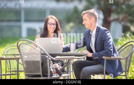 I colleghi di lavoro maschili e femminili discutono del lavoro su un notebook aperto e una tazza di caffè da asporto all'aperto. Foto Stock