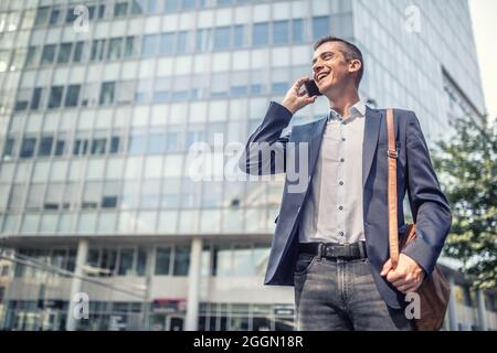 Abbigliamento casual business per l'uomo che parla su un telefono cellulare di fronte all'edificio ufficio sorridente. Foto Stock