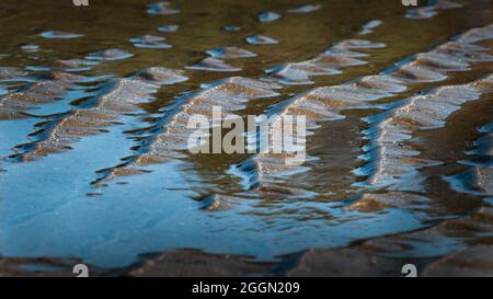 Motivi di sabbia e acqua di mare blu a bassa marea sulla spiaggia Foto Stock