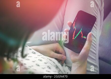 Mano femminile con smartphone trading stock online a casa. Concetto di business e investimento, doppia esposizione Foto Stock