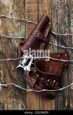 Sparatutto Cowboy 6, pistola con fondina intrappolata in filo metallico, su sfondo di legno. (la vecchia copertina del libro occidentale)? Foto Stock