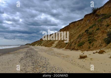 Vista lungo la riva a Cove Hythe con la scogliera di sabbia erodente e le scure nuvole tempestose. Foto Stock