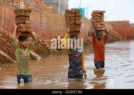 Un migrante del Bangladesh tiene blocchi di mattoni sopra la testa per trasportarlo sull'altro lato del fiume in un campo di mattoni a Dhaka. Circa 400,000 migranti a basso reddito arrivano a Dhaka ogni anno per lavorare a brickfields, nella fabbrica di mattoni milioni di mattoni vengono bruciati anche se questo influisce sull'ambiente in Bangladesh. Il 1 settembre 2021 a Munshiganj City, Bangladesh. (Foto di Harun-or-Rashid / Eyepix Group) Foto Stock