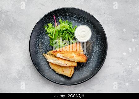 Vista dall'alto di una sottile crepe ripiena di formaggio fuso e prosciutto su un piatto Foto Stock