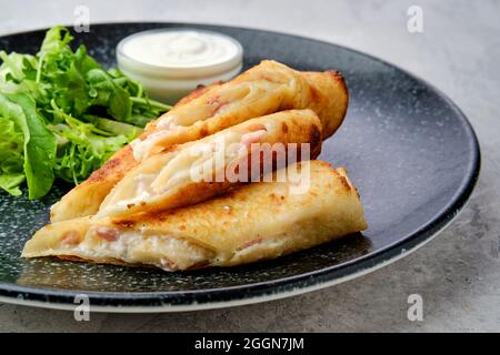 Primo piano di una sottile crepe ripiena di formaggio fuso e prosciutto su un piatto Foto Stock