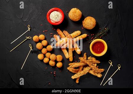 Allsorts di snack fritti con due diverse salse su sfondo nero. Close-up. Vista superiore Foto Stock