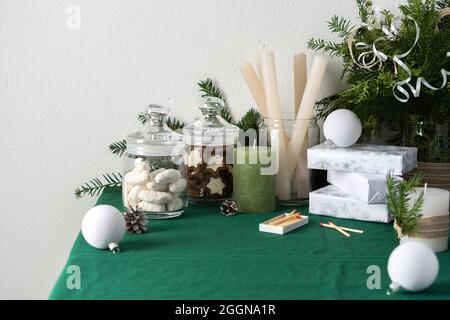 Tavolo natalizio o di Capodanno decorato per le feste, rami di thuja e abete rosso, candele e palline bianche di Natale, biscotti in un vaso, scatole regalo Foto Stock