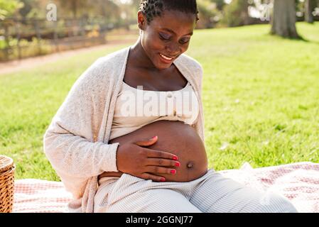 Felice donna nera incinta che tocca il ventre Foto Stock