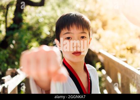 Ritratto di un giovane giocatore giapponese di karate in posizione di attacco o difesa vestito con il suo tae kwon ufficiale do kimono. Pugni forti e aggrappati per il combattimento Foto Stock