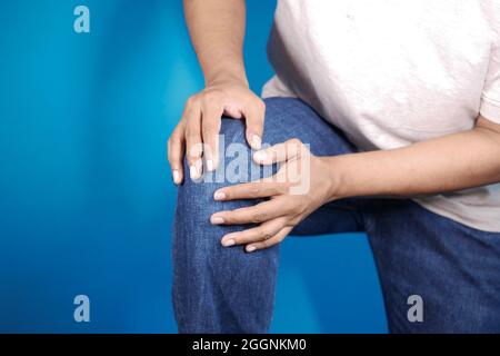 giovane uomo che tiene il ginocchio per aver sofferto dolore articolare su sfondo blu Foto Stock
