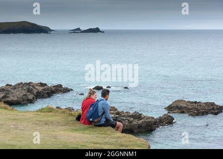 Una coppia in vacanza seduta insieme sulla costa a Newquay che si affaccia sul Mar Celtico. Foto Stock