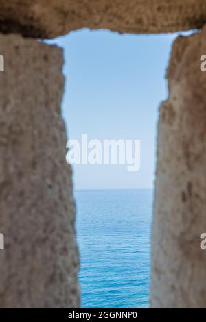 Scatto verticale di un mare azzurro cristallino visto attraverso il foro di un muro di pietra Foto Stock