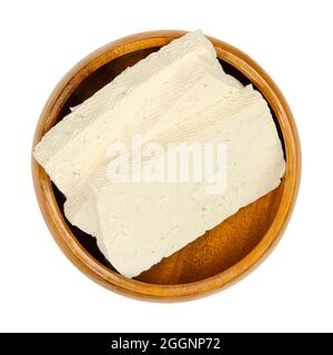 Fette di tofu bianco, in una ciotola di legno. Cagliata di fagioli a fette, latte di soia coagulato, pressata in blocchi bianchi di diversa morbidezza. Foto Stock