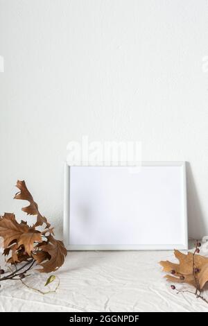 Casa decoratore moccap, quadro vuoto cornice vicino bianco dipinto muro di cemento, rami con foglie asciutte Foto Stock