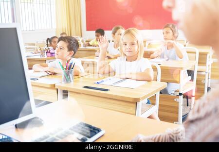 Scuola premessa alzando la mano per rispondere durante la lezione Foto Stock