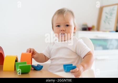 Biondo biondo con occhi blu che gioca con figure geometriche in plastica. Sviluppo del motore del bambino all'asilo Foto Stock