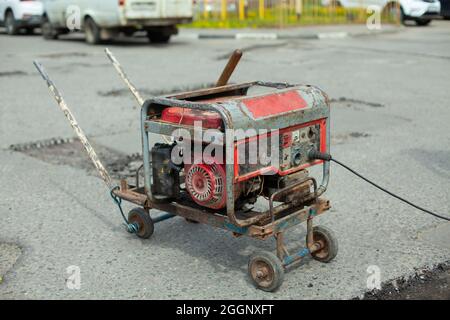 Generatore di benzina di elettricità. Alimentazione all'utensile elettrico. Generatore sulla strada per la riparazione stradale. Foto Stock