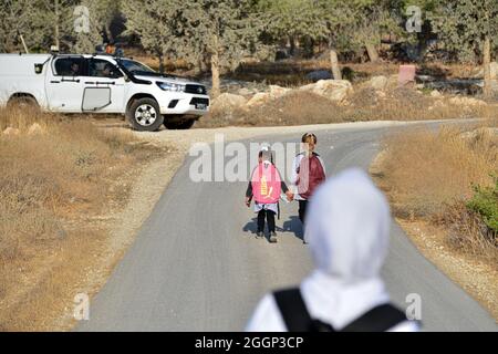 Dal 2004 i bambini del villaggio di Tuba stanno andando a scuola nel vicino villaggio di AT-Tuwani, 2.6 km di distanza - mentre sono stati condotti da un attivista ebraico e un veicolo delle forze di difesa israeliane per proteggerli dagli attacchi violenti da parte dei coloni ebrei religiosi dall'avamposto illegale di Maon Farm, che si trova sul loro cammino verso la scuola. Palestina/Israele, a sud di Hebron. 31 agosto 2021. (Foto di Matan Golan/Sipa USA) Credit: Sipa USA/Alamy Live News Foto Stock