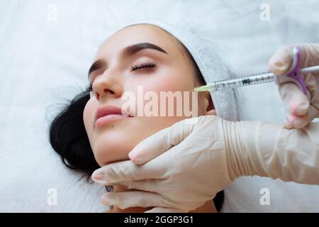 Sollevamento del sorriso e aumento del labbro. Medico estetista mani che fanno la procedura di bellezza al viso femminile con siringa. Bocca della giovane donna contornata con Foto Stock