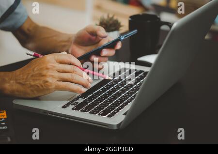 Mano che tiene una matita, calcolatrice e telefono cellulare, tastiera del computer sulla scrivania. Foto Stock