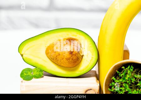 Avocado creativo, banana e micro verde equilibrio legno stand e podi., sfondo bianco, equilibrio sano cibo. Concetto di nutrizione equilibrata Foto Stock